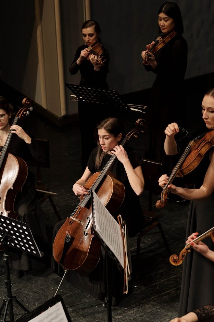 A professional orchestra rehearsing string instruments on a dimly lit stage.